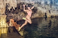 a woman jumping into the water in a cave
