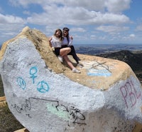 two women sitting on top of a large rock with graffiti