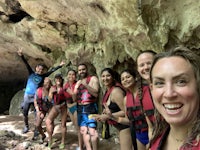 a group of people in life jackets pose in front of a cave