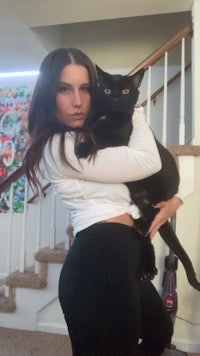 a woman holding a black cat in front of stairs