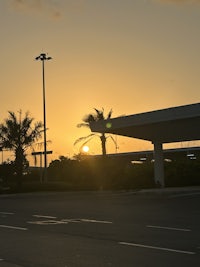 the sun is setting over a parking lot with a palm tree in the background