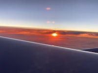 an airplane wing with the sun setting behind it