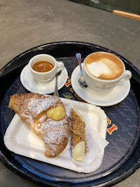 a black tray with a pastry and a cup of coffee